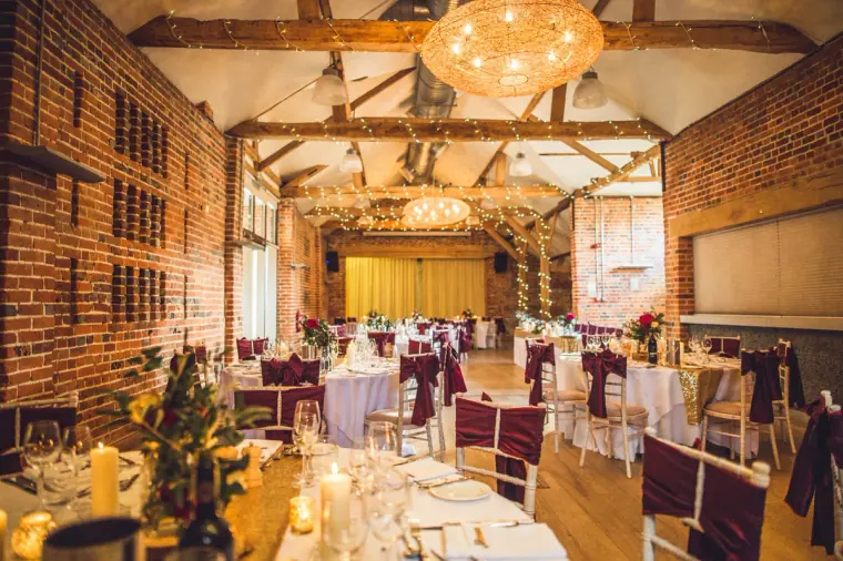 Wide view of the candlelit barn with round tables and glowing chandelier, Wasing Park