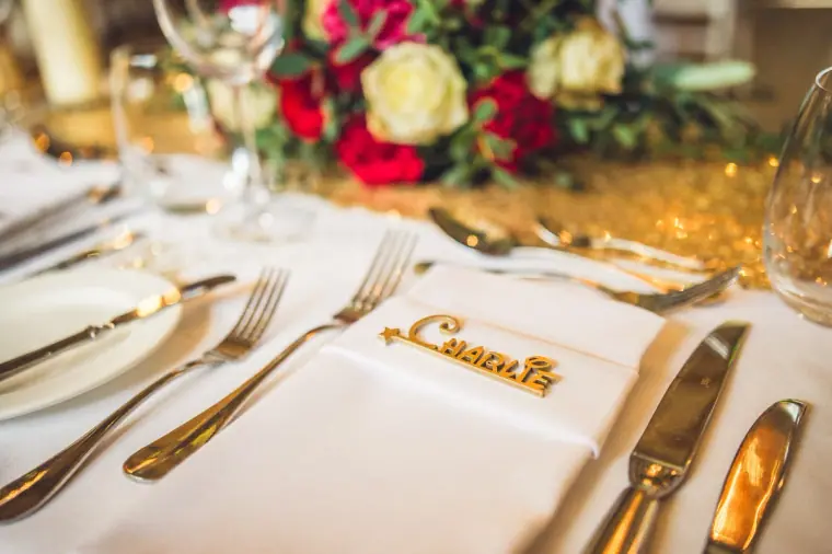 Gold cutlery and a gold name place card on a white napkin beside red roses