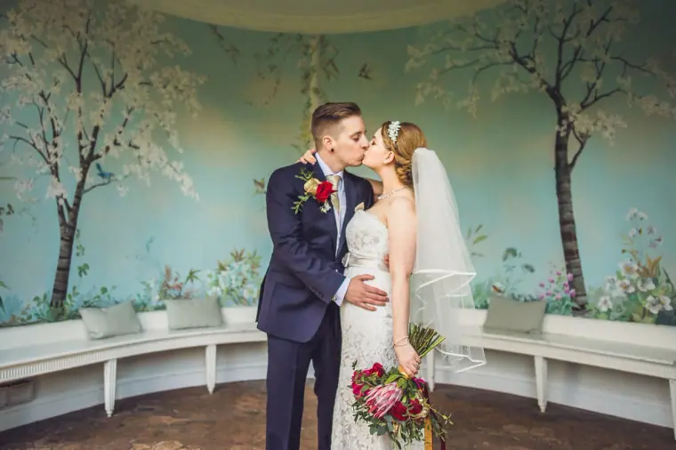 Sarah and Charlie kissing in a painted garden pavilion at Wasing Park