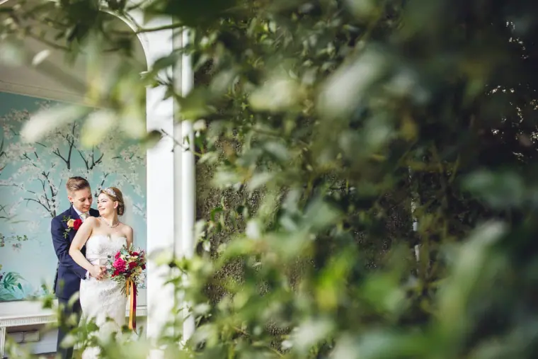 Couple glimpsed through foliage inside a white garden pavilion