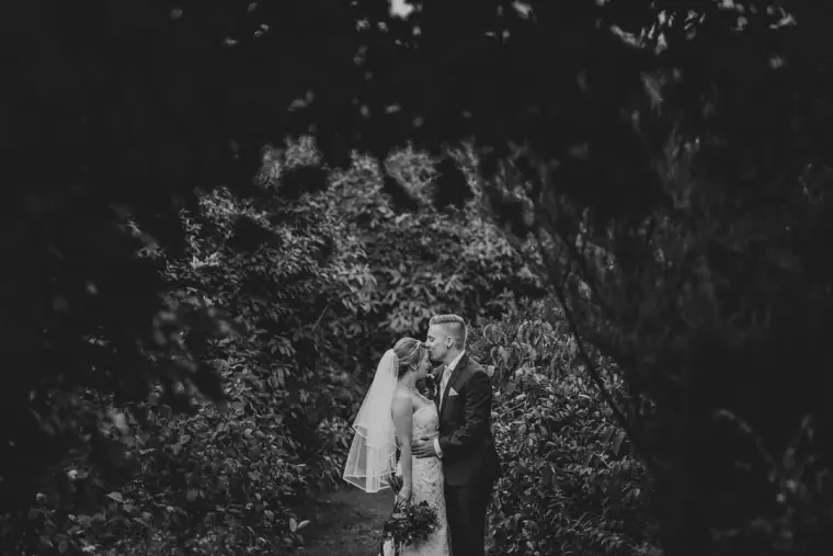 Black-and-white photo of the couple kissing among dark foliage