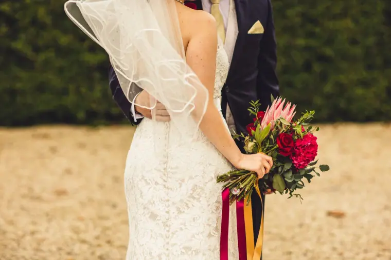Close-up of the bride's lace dress and red protea bouquet with ribbons