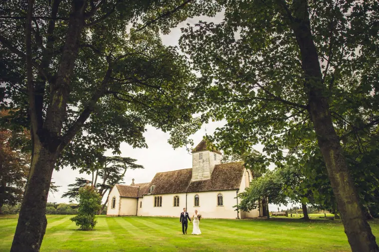 Couple walking on the lawn before the white church at Wasing Park