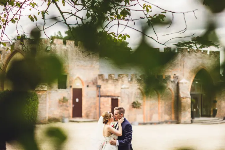 Sarah and Charlie embracing before the old brick walls, framed by leaves
