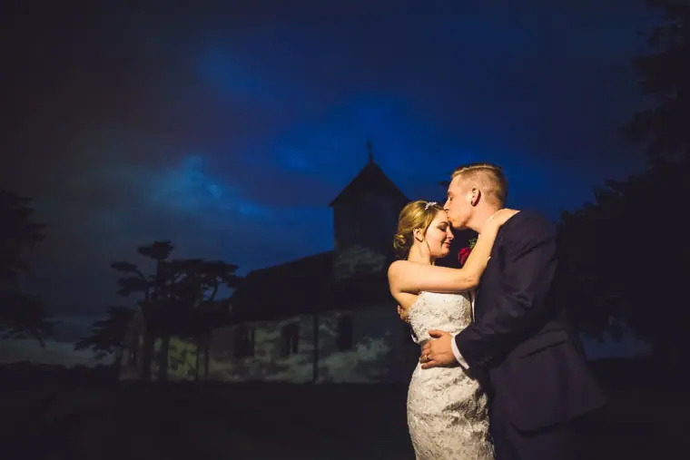 Couple kissing against a deep blue night sky by the church at Wasing Park