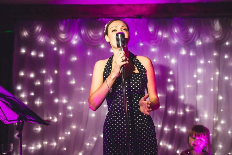 Singer in a polka-dot dress performing in front of a purple-lit starry curtain