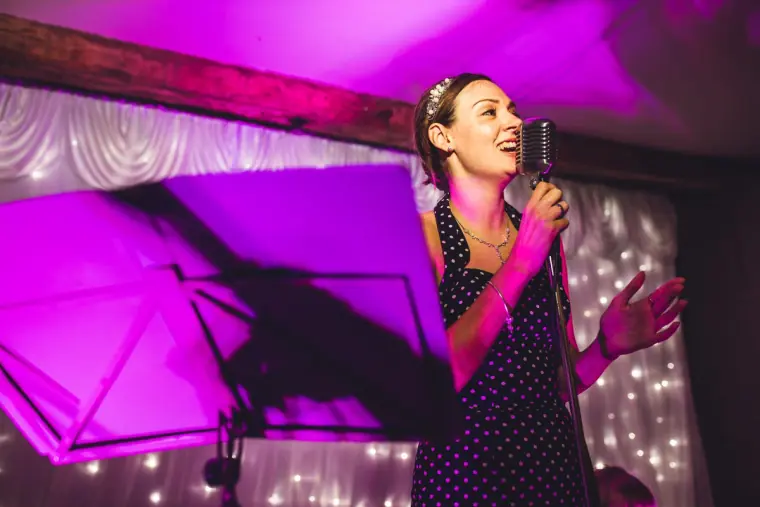 Singer smiling into a vintage microphone under purple stage lights