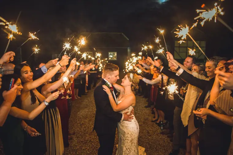 Sarah and Charlie kissing in a tunnel of guests holding sparklers