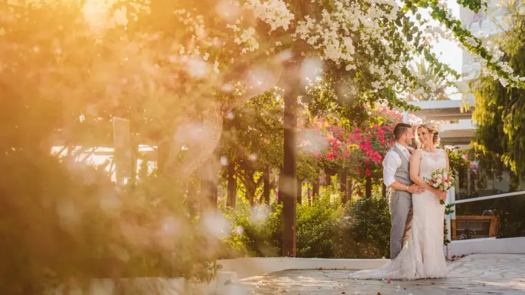Kellie and Simon embracing among sunlit trees and bougainvillea, Nissi Beach, Ayia Napa
