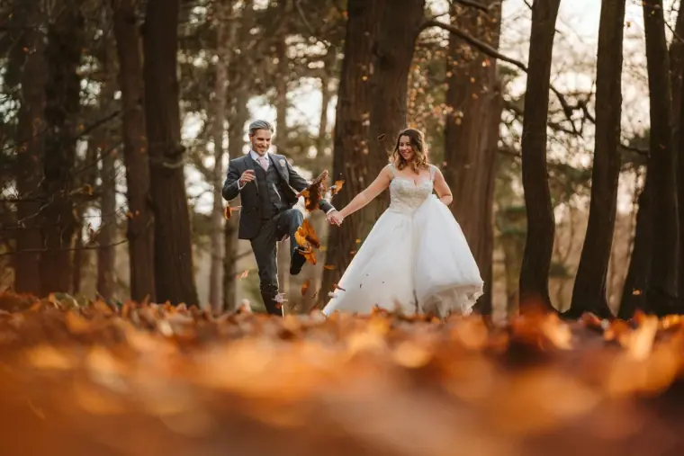 Ellie laughing as James kicks up autumn leaves in a pine wood