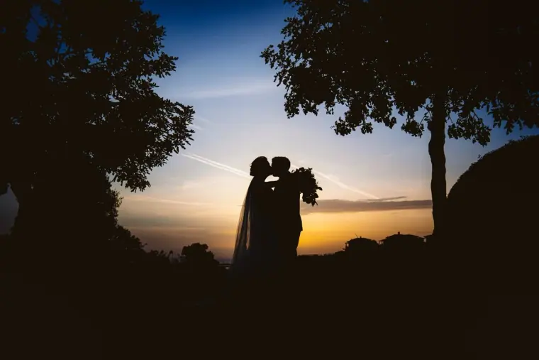 Silhouette of Lauren and Ray kissing at dusk between trees, Aphrodite Hills