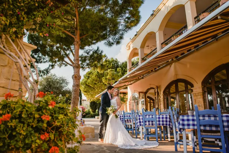 Couple kissing beside a terrace with blue chairs and gingham tablecloths