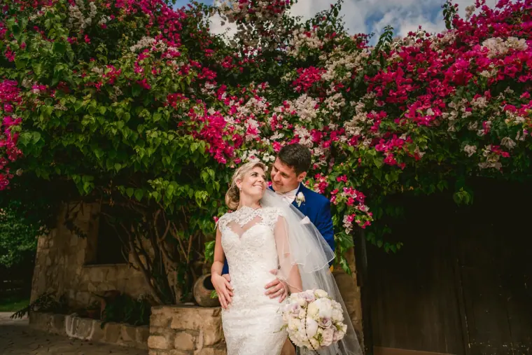 Bride and groom smiling beneath a wall of pink bougainvillea