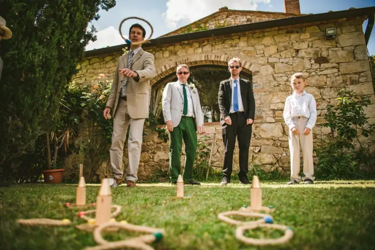 Men in summer suits playing ring toss on the lawn by a stone building