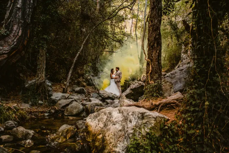 Couple standing in a misty, sunlit gorge beside a rocky stream