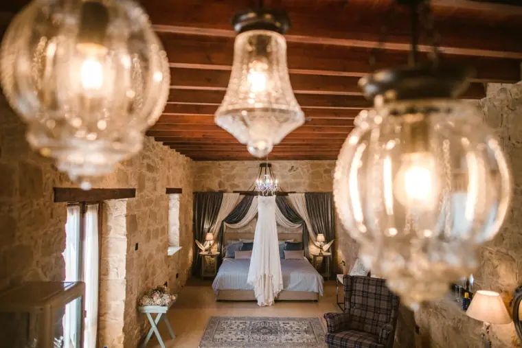 Wedding dress hanging in a stone-walled suite seen past glowing glass lanterns