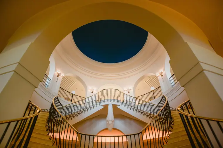 Couple on a curved double staircase beneath a domed skylight, seen from below