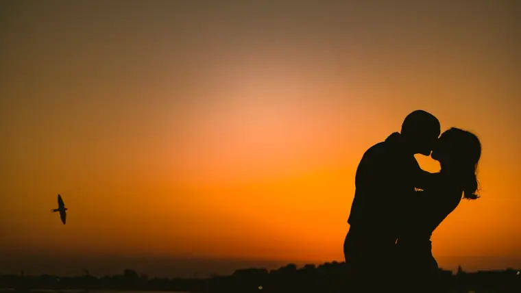 Silhouette of a couple kissing against a deep orange sunset sky