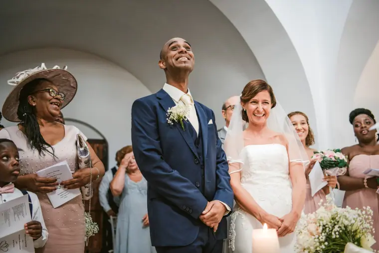 Groom gazing upwards and the bride smiling during a ceremony in a white chapel