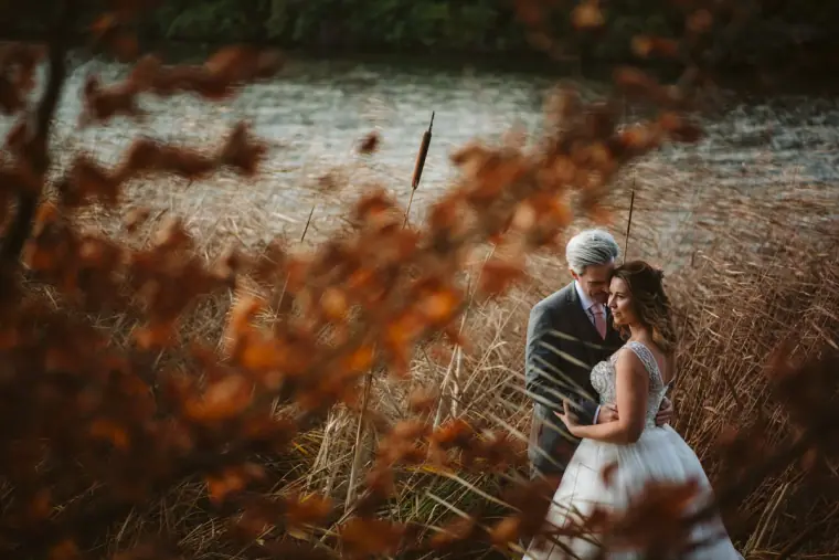 Couple embracing beside a lake, framed by autumn leaves