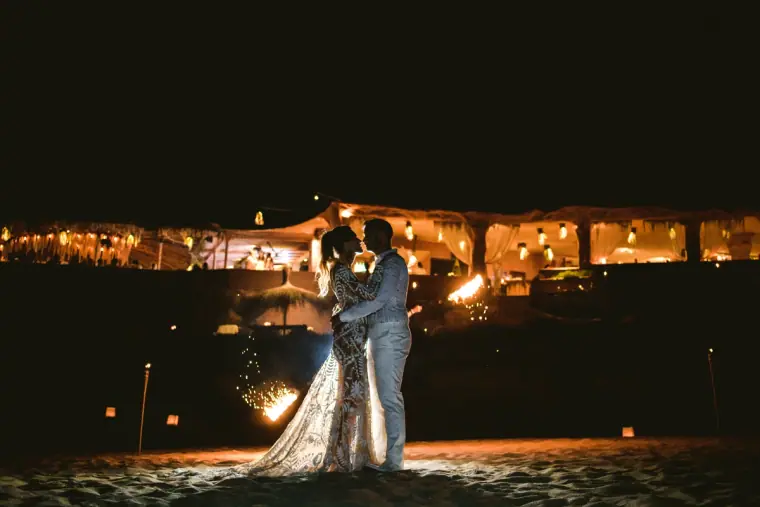 Bride and groom embracing at night before a lantern-lit marquee