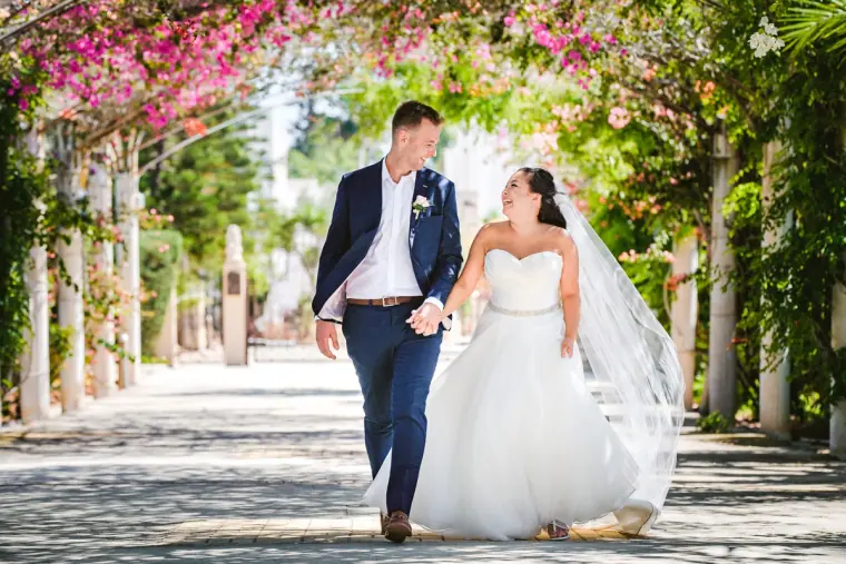 Bride and groom walking beneath a bougainvillea-covered pergola walkway