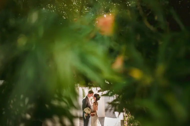 Couple glimpsed through soft-focus green foliage by a white building