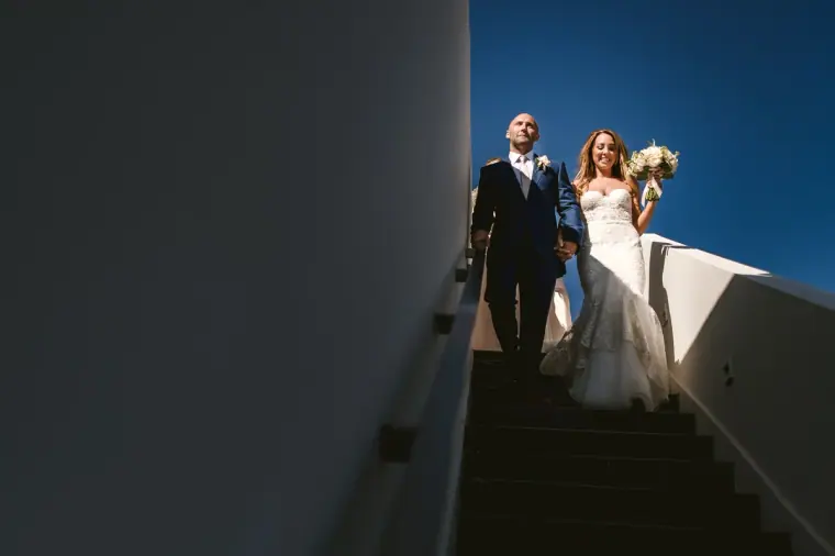 Bride and groom walking down outdoor steps against a deep blue sky