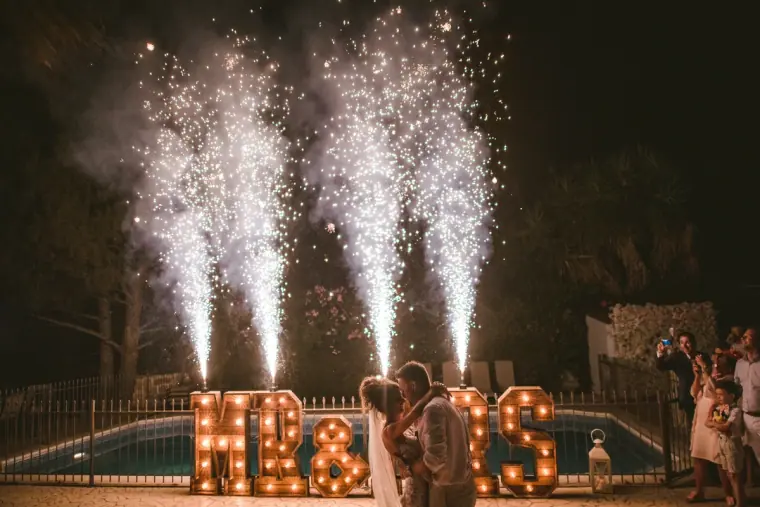 Couple kissing behind light-up MR & MRS letters as sparkler fountains fire