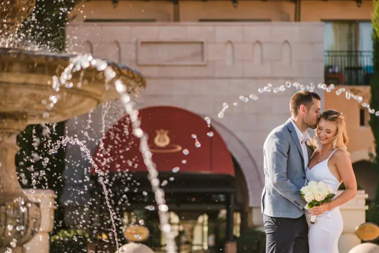 Couple embracing beside a splashing fountain in front of a grand building