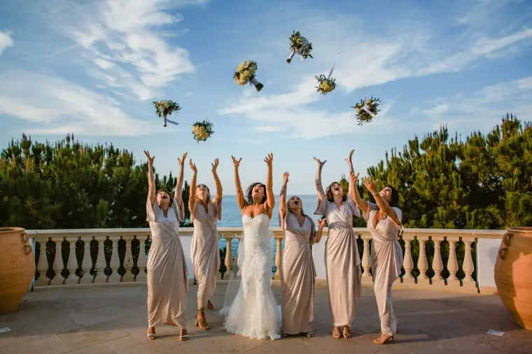 Bride and bridesmaids tossing their bouquets into the air on a sea-view terrace