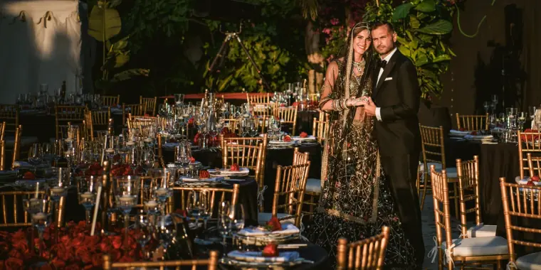 Bride and groom standing among long candlelit dinner tables in a garden