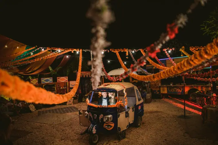 Tuk-tuk beneath orange garlands and string lights at a night-time party