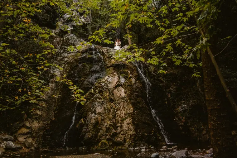 Couple dwarfed by a mossy waterfall in a lush green gorge