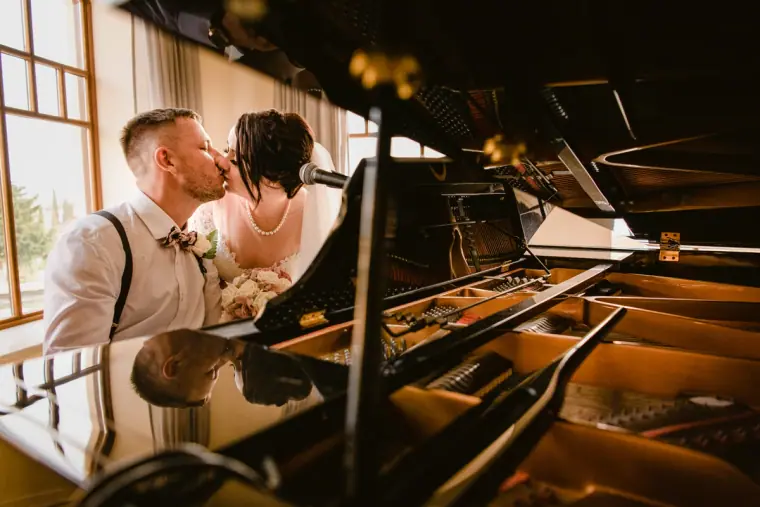 Groom and bride kissing behind an open grand piano