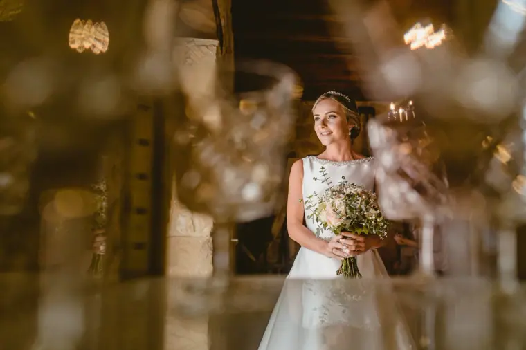 Bride holding a white bouquet, framed by glinting glassware