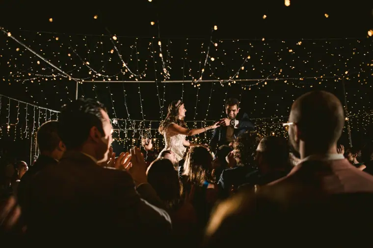 Couple dancing under a canopy of fairy lights surrounded by guests