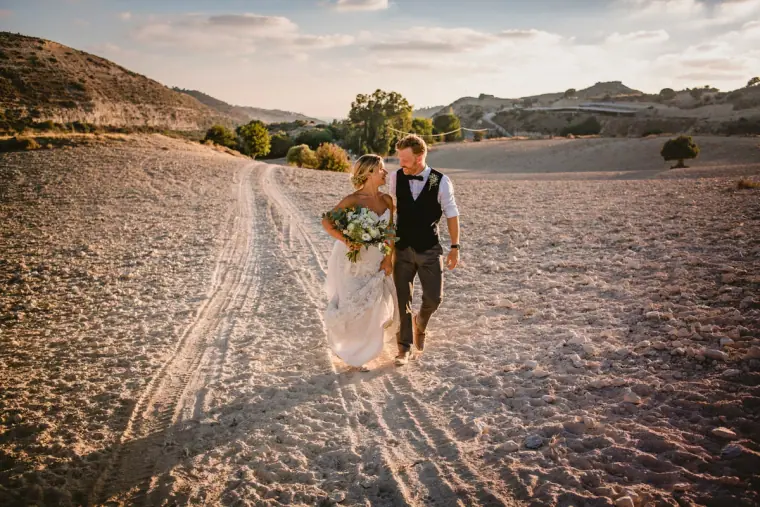Bride and groom walking along a sandy track through hills