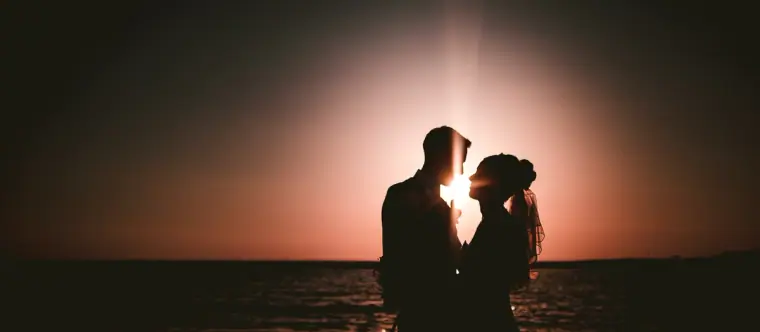 Silhouette of a couple face to face against a glowing sunset sea