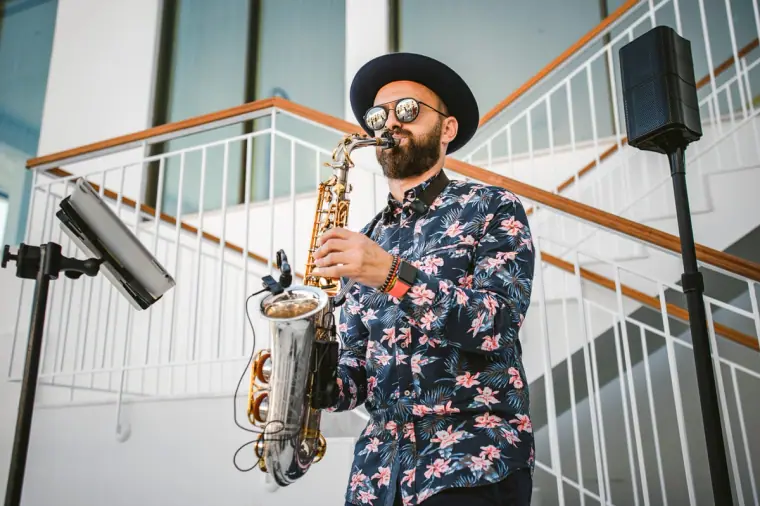 Saxophonist in a hat and floral shirt playing beside a white staircase at a wedding party