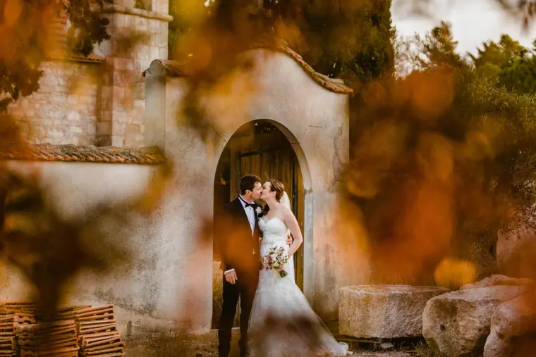 Couple kissing in the arched doorway of an old stone chapel, framed by autumn leaves