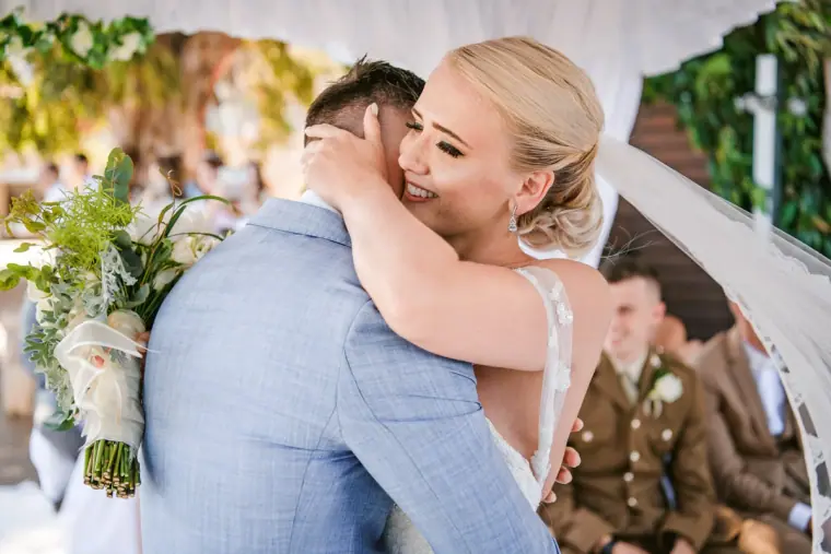 Bride hugging a guest in a blue suit, beaming with her bouquet in hand