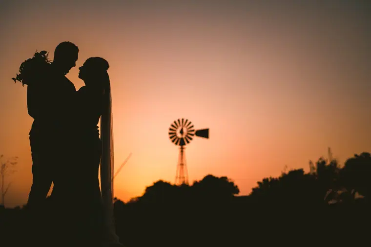 Silhouette of bride and groom kissing at sunset beside a windmill