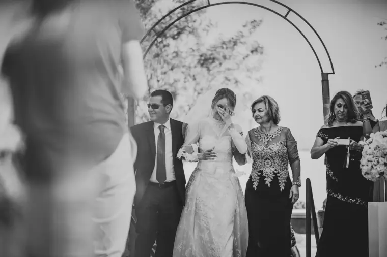 Black-and-white photo of a bride wiping a tear during the ceremony as guests look on