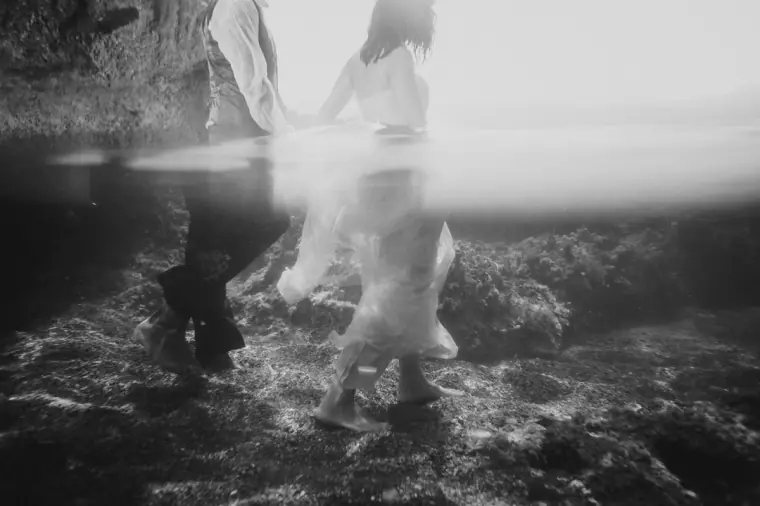 Black-and-white photo of the couple's feet on rocks at the water's edge