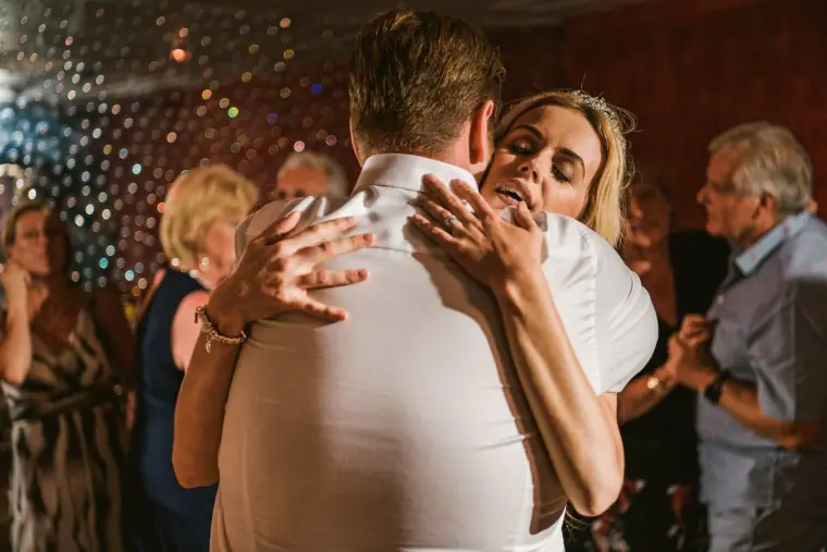 Bride hugging a guest on the dance floor beneath glittering lights
