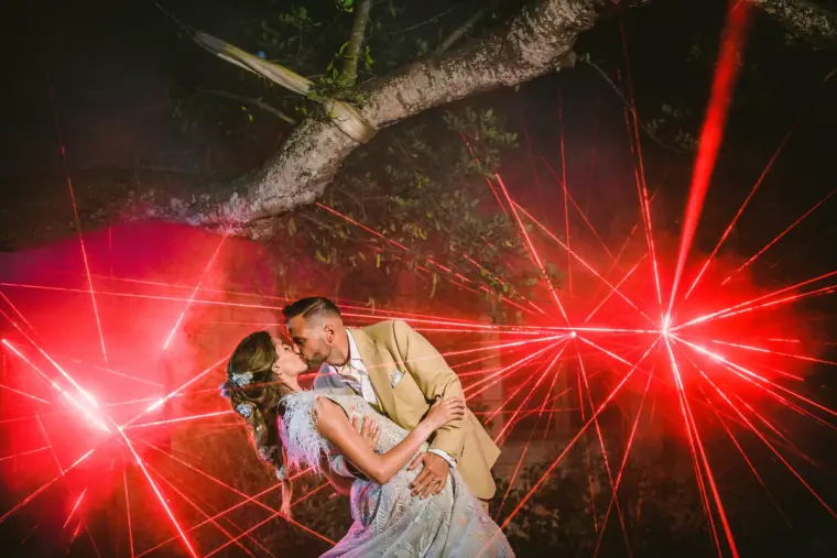 Groom dipping his bride for a kiss amid red laser beams at a night party