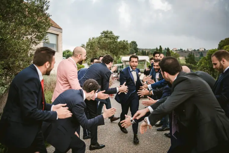 Groomsmen forming a tunnel of outstretched arms for the groom on a path