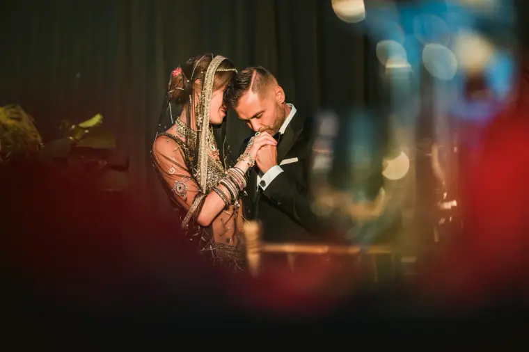 Groom kissing the forehead of his bride in a jewelled headpiece, framed by red blur