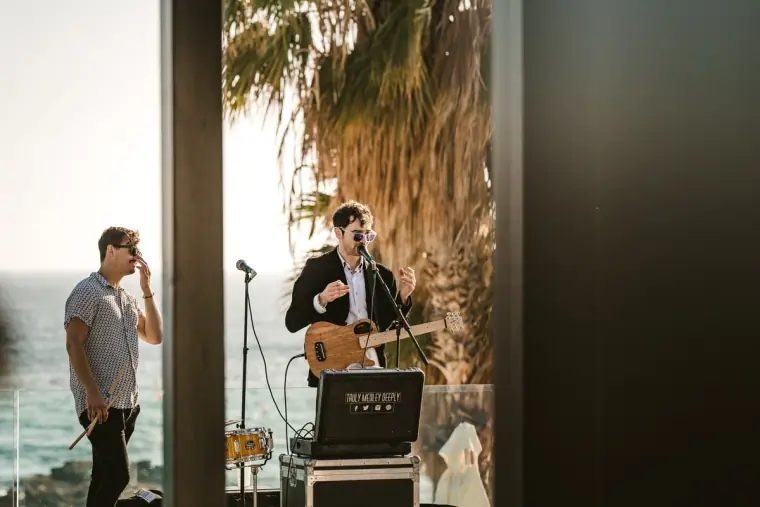 Guitarist singing at a microphone on a sunny terrace with sea views